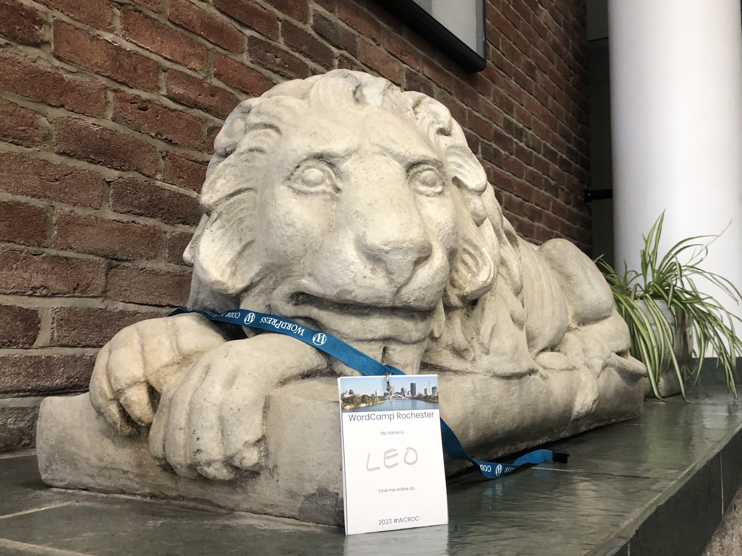 Statue of a lion wearing. Around it's neck is a WordCamp Rochester lanyard and name tag, named Leo.